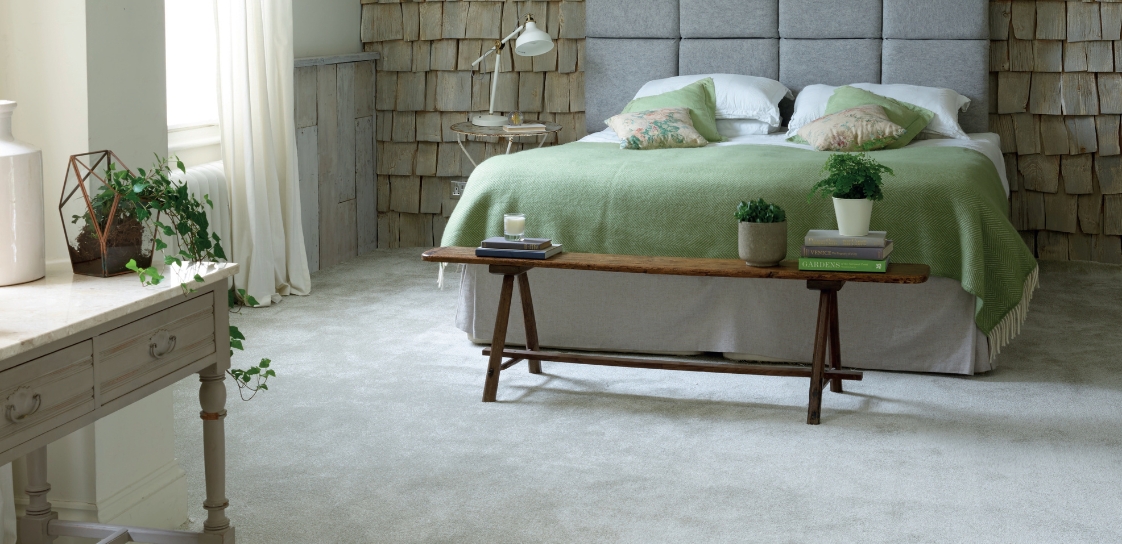 Neutral carpet, laid in a bedroom with wood cladded walls and coffee table at foot of bed.