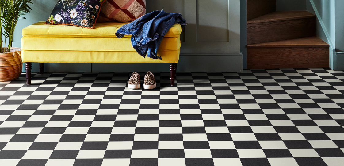 A black and white chequer tile effect vinyl in a hallway with staircase backdrop and yellow sofa