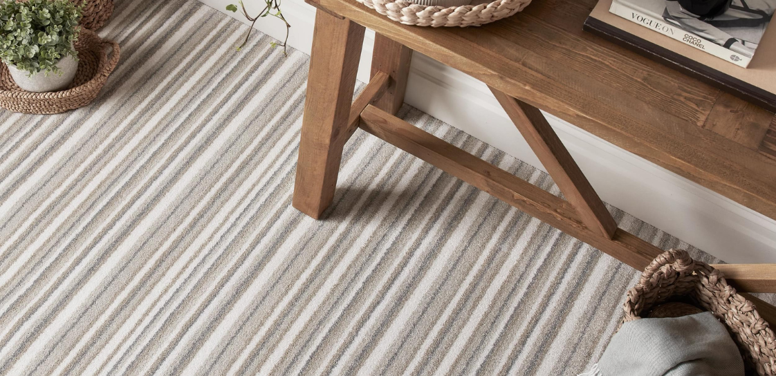 A neutral brown and grey stripe carpet with wooden side table, a plant and a candle