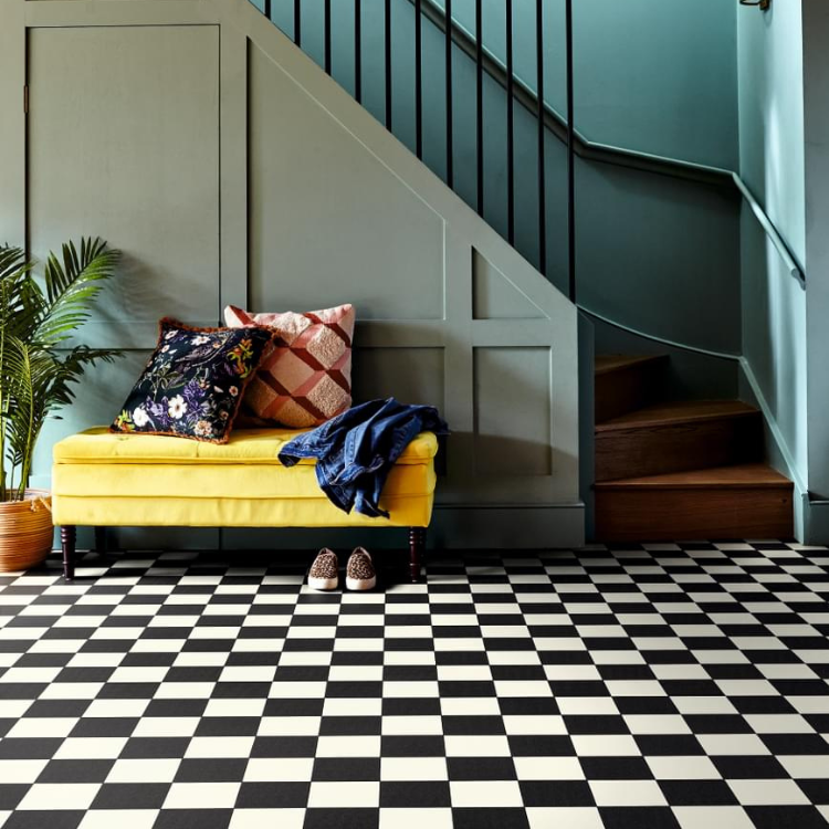 A black and white chequer tile effect vinyl in a hallway with staircase backdrop and yellow sofa