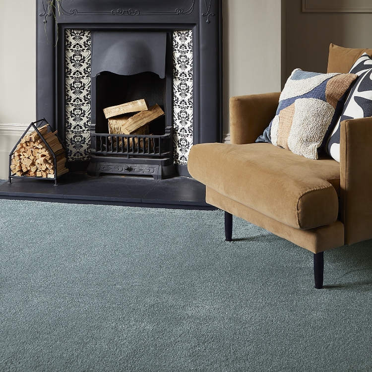A blue shade of carpet laid in a country style living area with mustard armchair and fireplace.