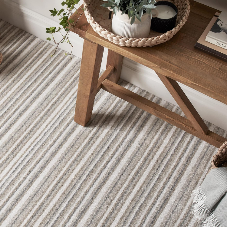 A neutral brown and grey stripe carpet with wooden side table, a plant and a candle