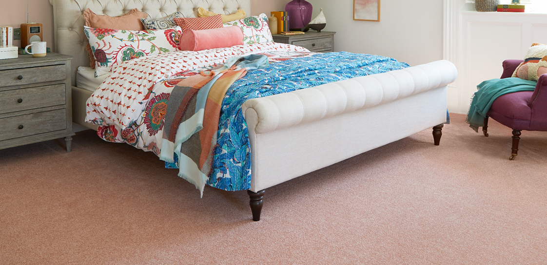 A pink bedroom with colourful bedspreads, white headboard and pink carpet