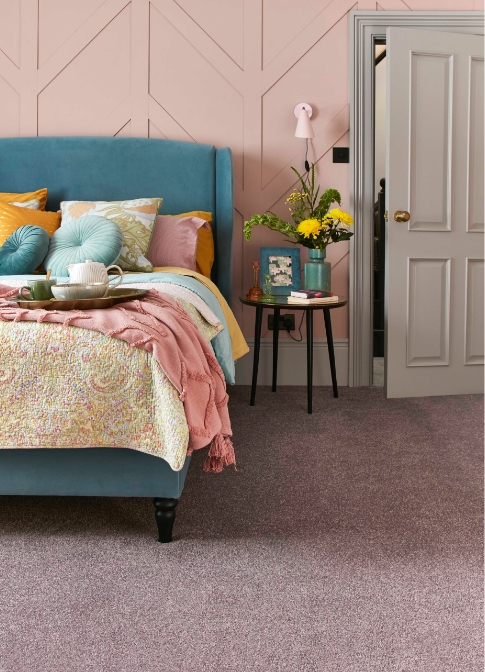 A blue bed is placed in front of a pink panelled wall. Colourful cushions and a pink carpeted floor.