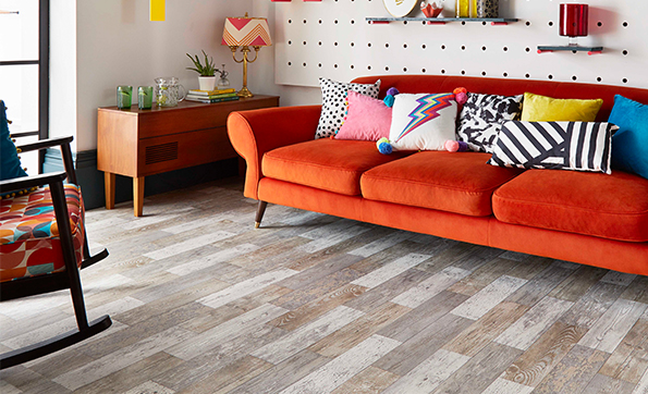 Wood effect vinyl flooring in a funky living room with red sofa and patterned cushions