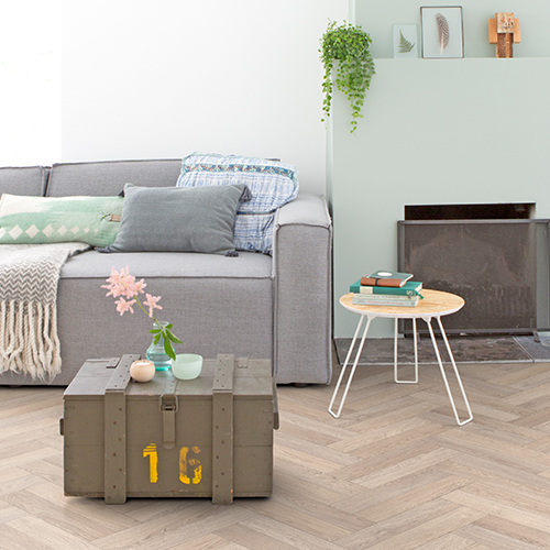 A living room with a light oak herringbone flooring, styled with a pastel coloured interior