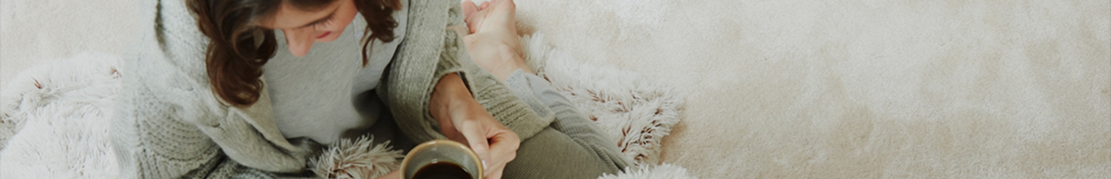 Barefoot woman sat on grey carpet floor, leaning on pink sofa